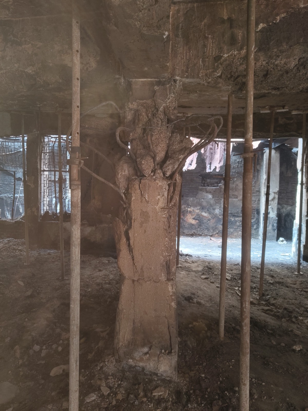 A fire-damaged concrete column with exposed bars, surrounded by steel props holding up the slab